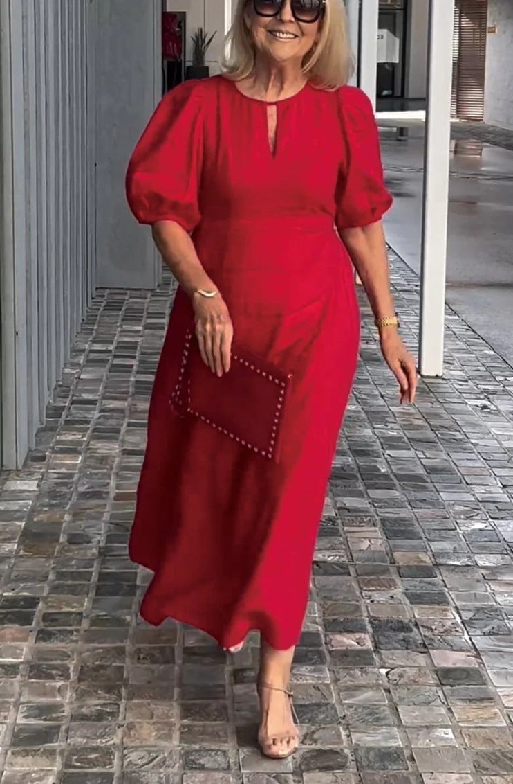 Woman in a red dress holding a matching clutch on a tiled pavement.