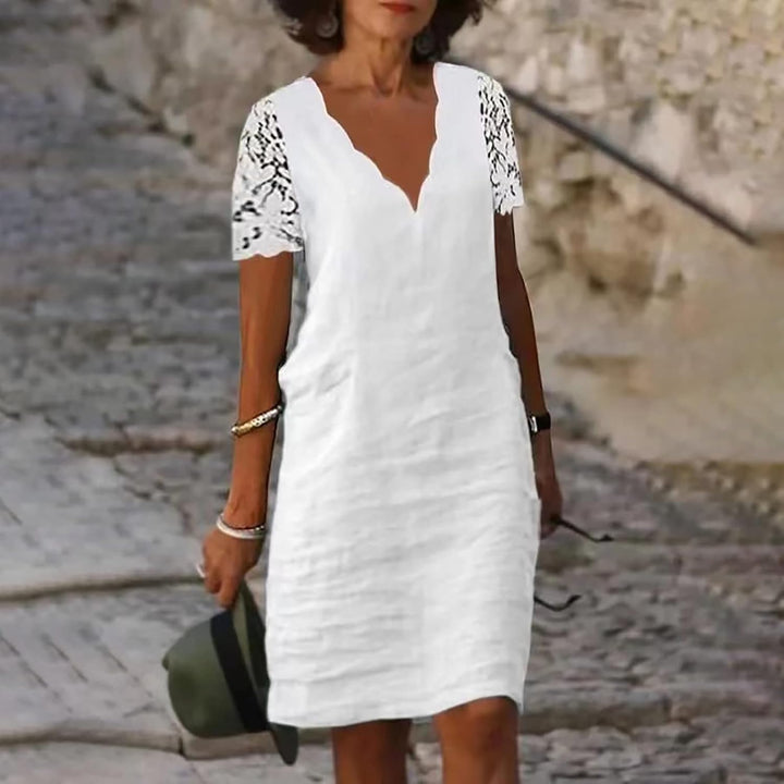 Woman wearing a white dress with lace sleeves against a stone wall background