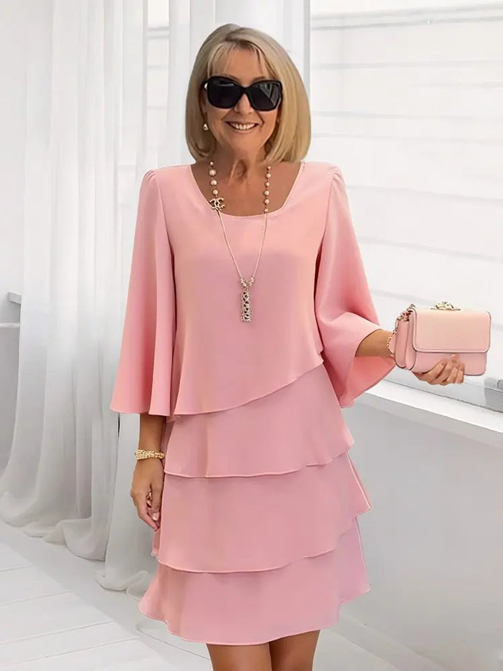 Woman wearing a pink dress with a matching handbag indoors.