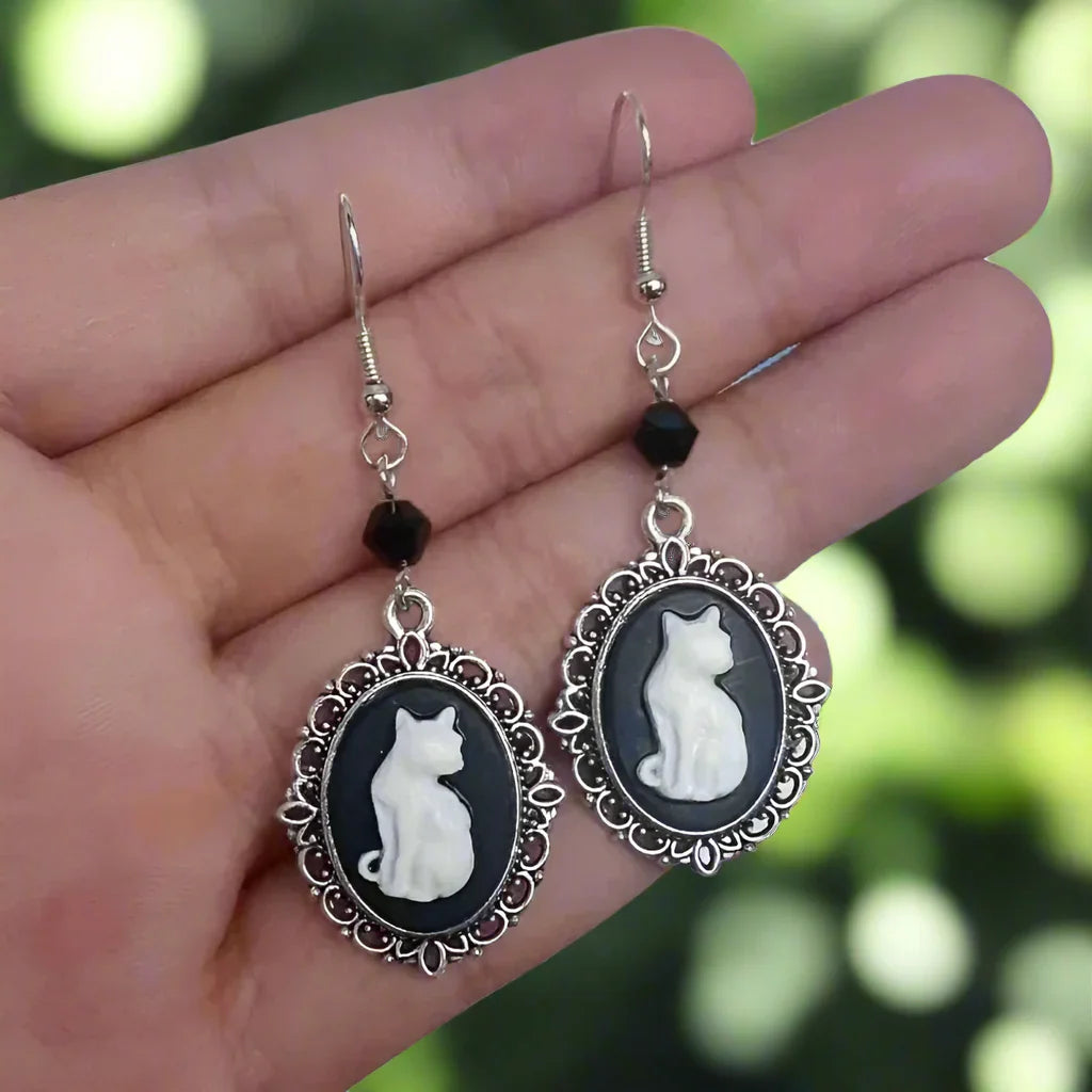 Cameo earrings with cat designs held in a hand against a blurred green background
