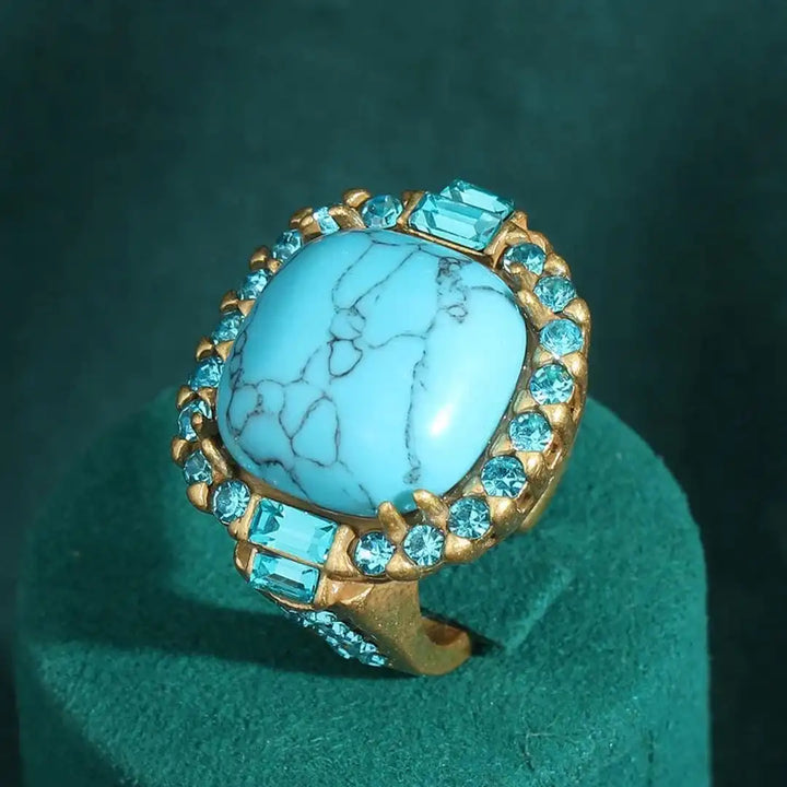 Gold ring with a large turquoise stone and smaller blue stones on a green background