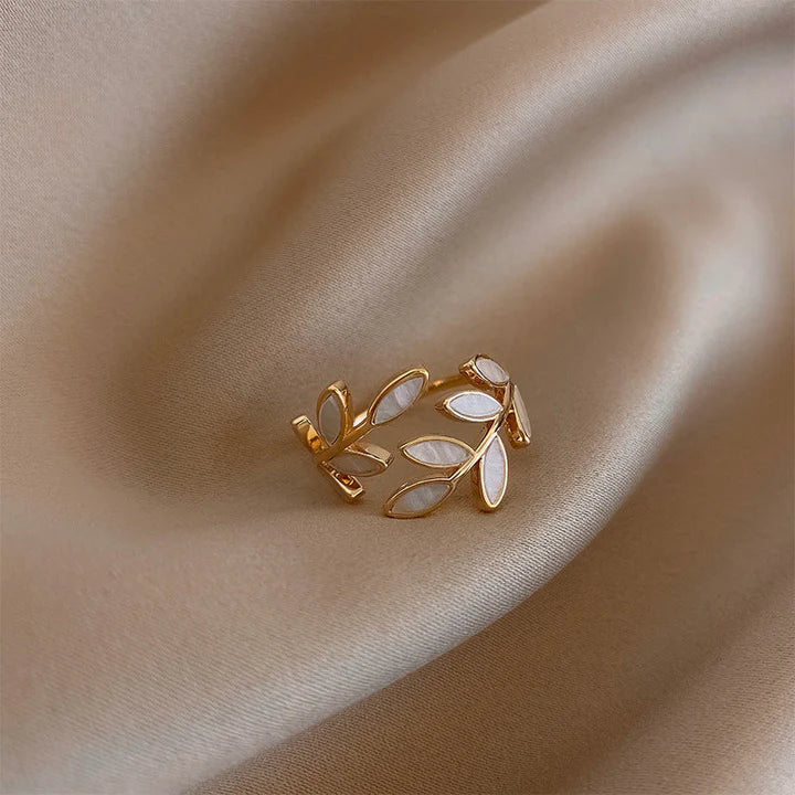 Gold ring with leaf designs on a beige fabric background