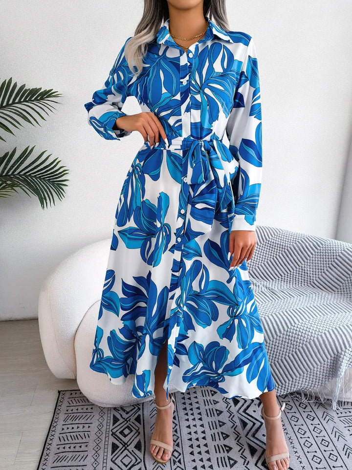 Woman wearing a blue and white floral dress in a room with a plant and chair.