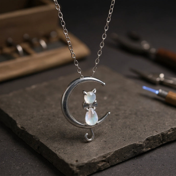 Silver necklace with a cat and moon design on a dark surface