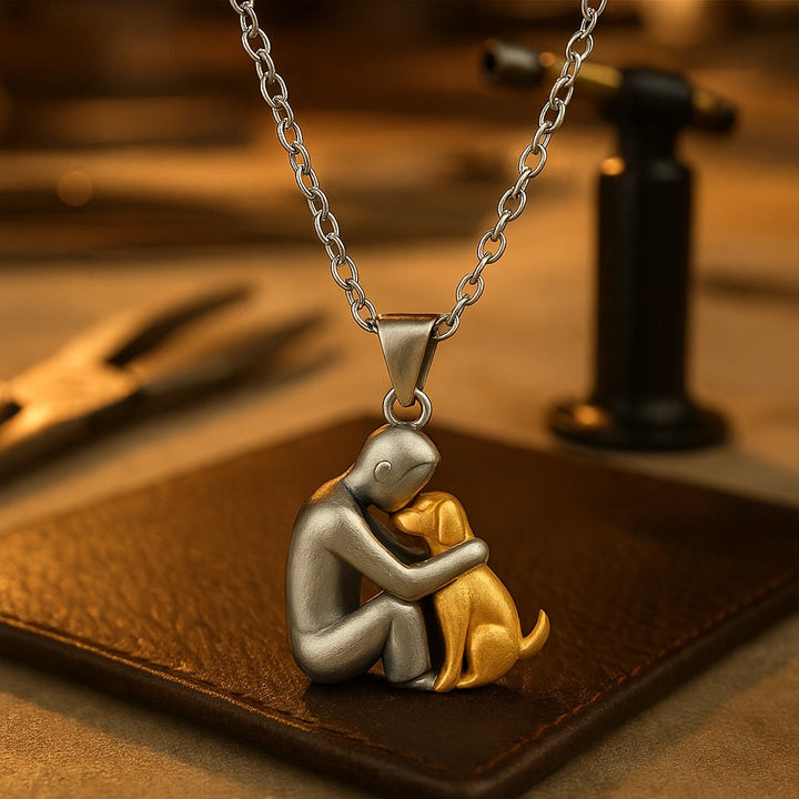 Necklace with a silver and gold pendant of a person hugging a dog on a brown leather surface.