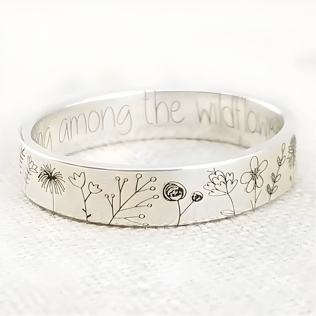 Silver bracelet with floral designs and engraved text on a white background