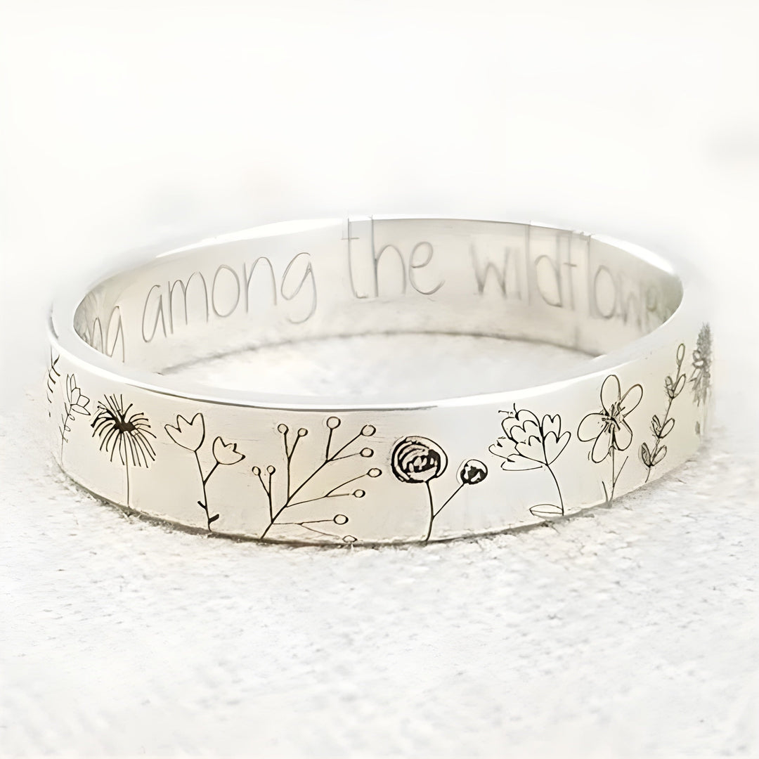 Silver bracelet with floral designs and engraved text on a white background