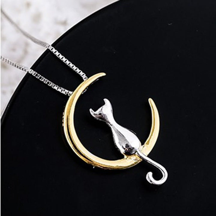 Gold crescent moon and silver cat pendant on a black background