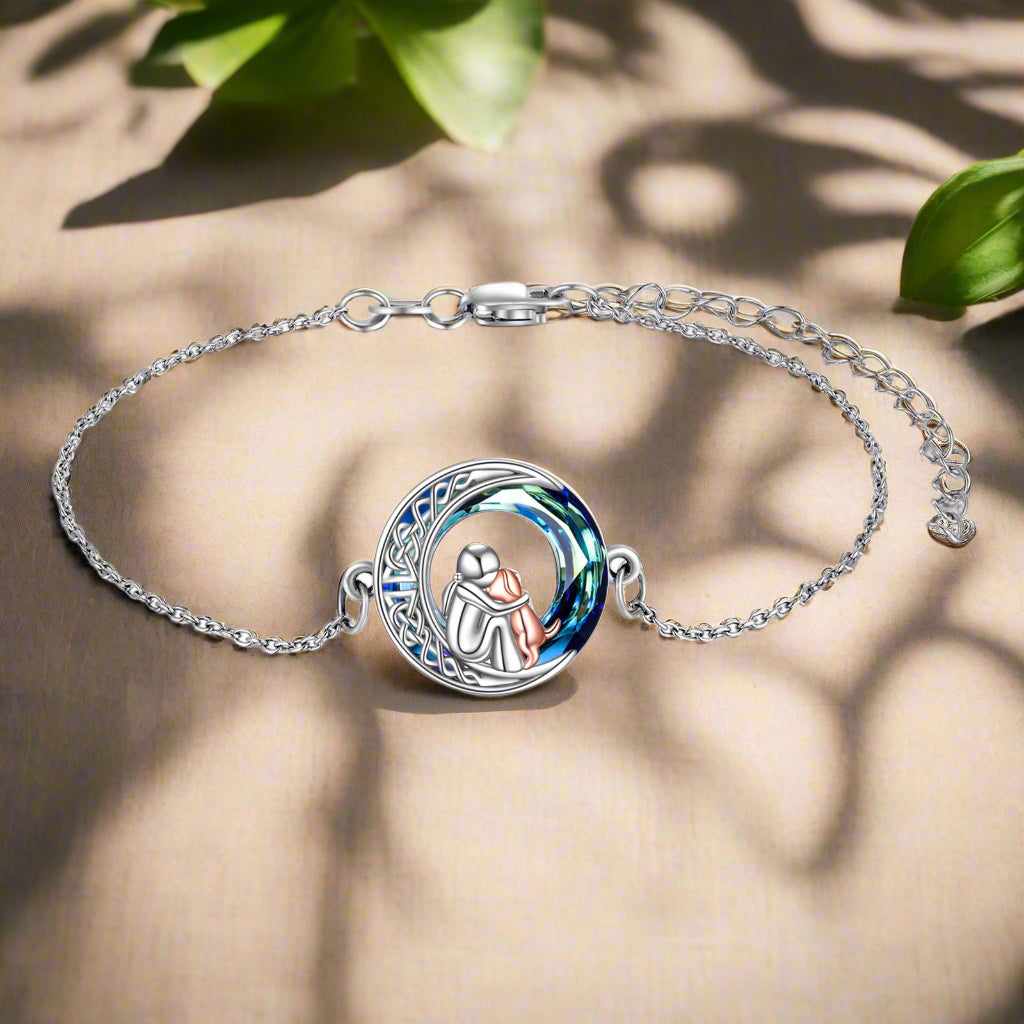 Silver bracelet with a circular design featuring two figures on a beige surface with green leaves.