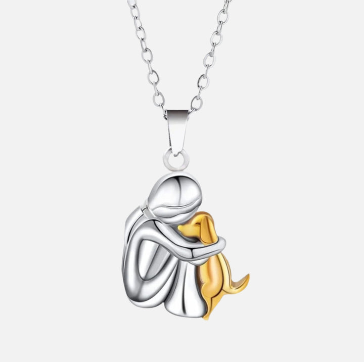 Silver and gold pendant of a person hugging a dog on a white background