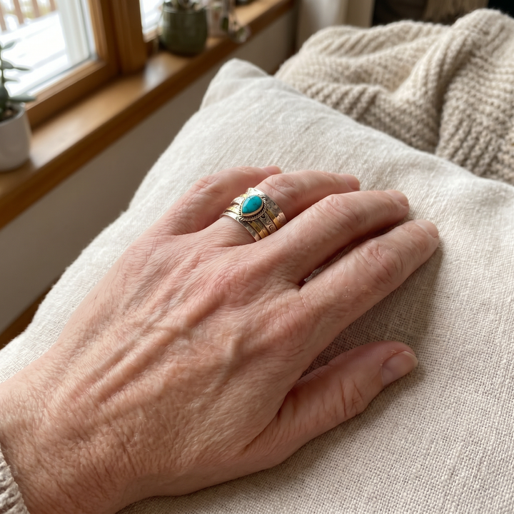 Hand wearing a ring with a turquoise stone on a textured surface