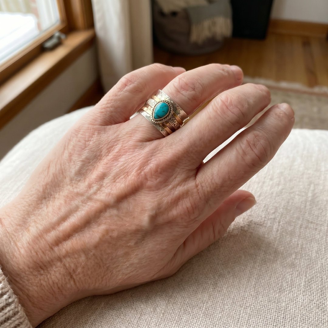 Hand wearing a ring with a turquoise stone on a neutral background