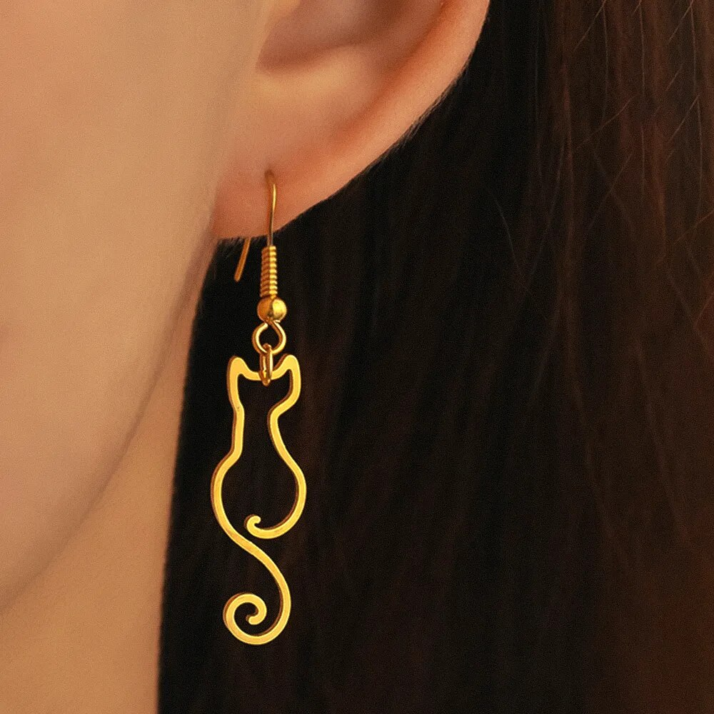 Gold cat-shaped earrings worn by a person with black hair.