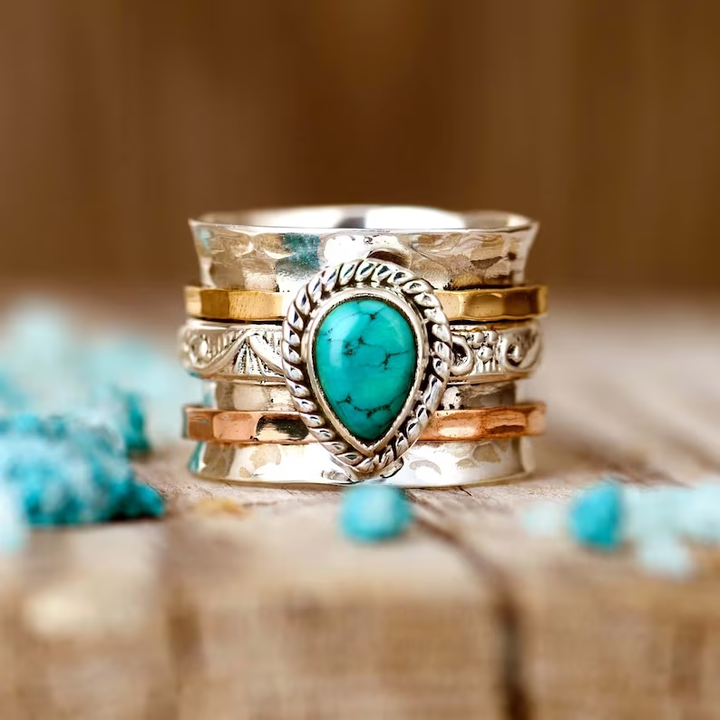 Stack of silver and gold rings with a turquoise stone on a wooden surface.