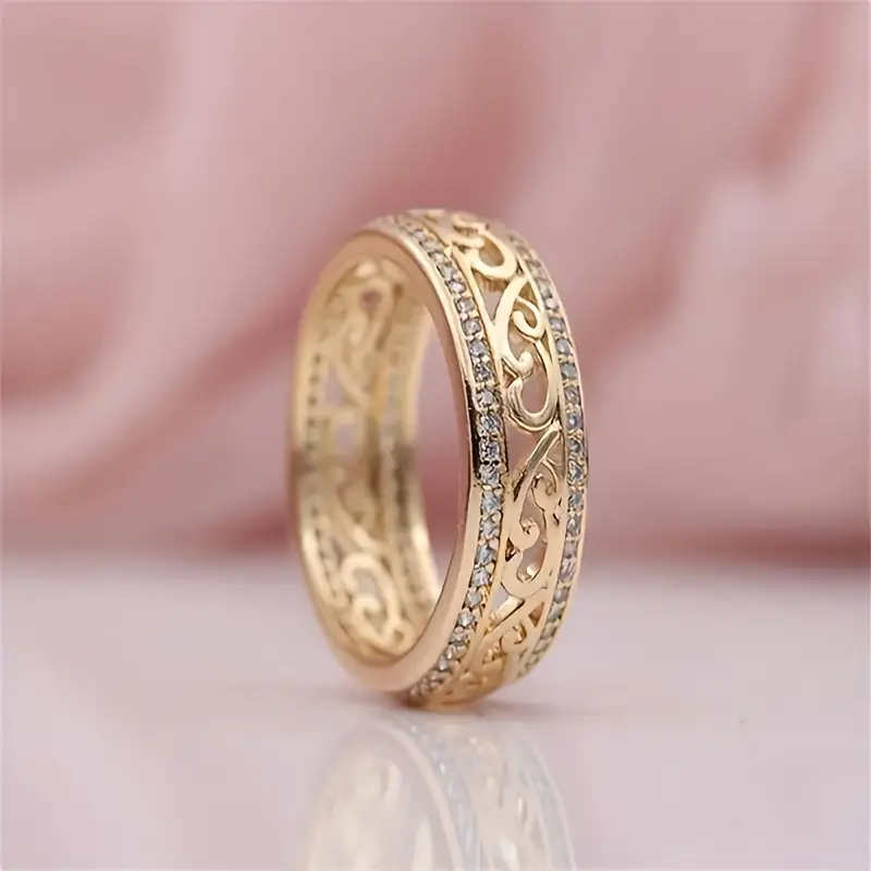 Gold ring with intricate design on a pink fabric background