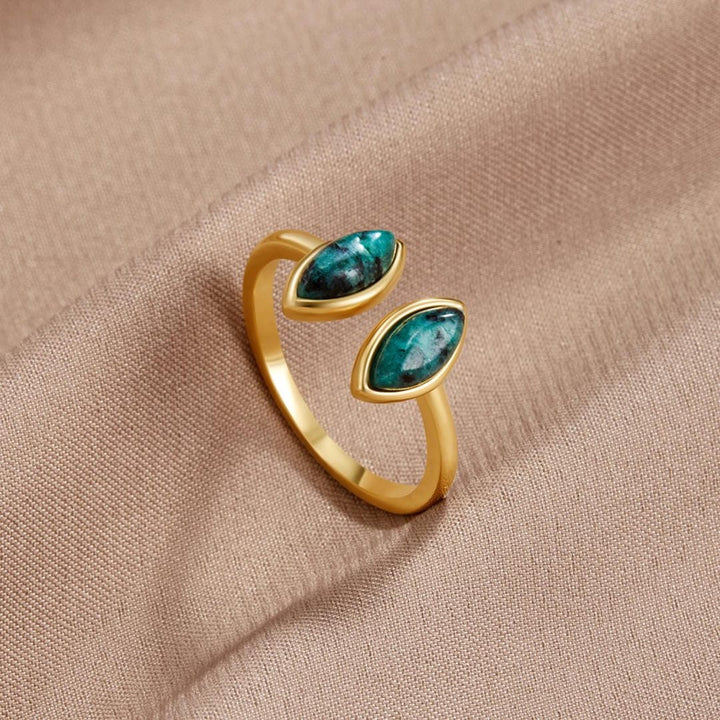 Gold ring with green gemstones on a beige fabric background
