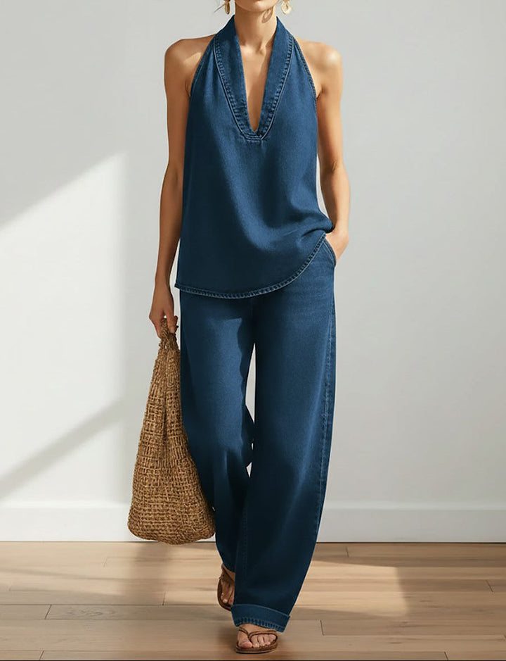 Woman wearing a blue halter top and wide-leg pants holding a woven bag indoors.