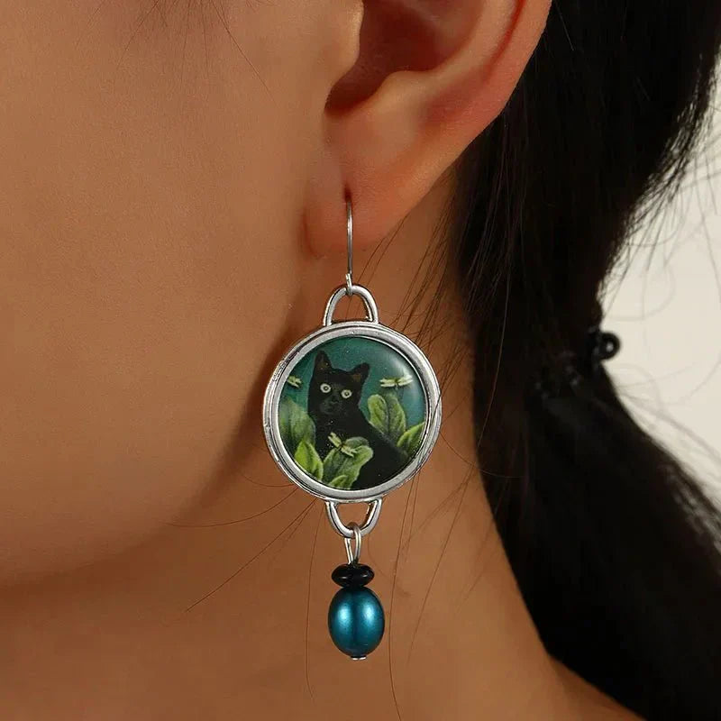 Earring with a black cat design on a green background worn by a person.